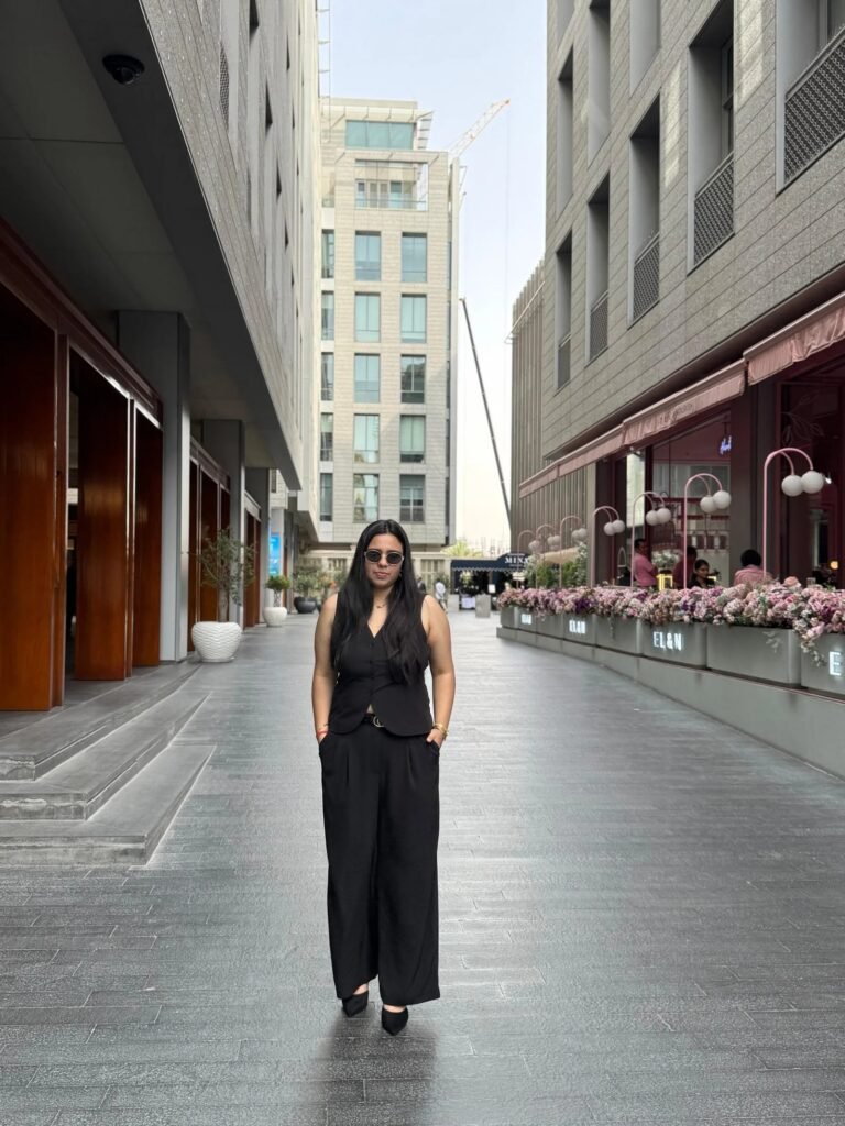 Woman in black outfit walks on urban street between buildings
